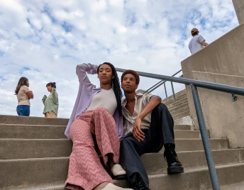 A young, Black woman and man sitting on concrete stairs. In the background, two women are outlined in a white silhouette.