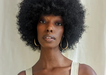 A young, Black woman with an afro hairstyle wearing a tank top and looking into the camera.